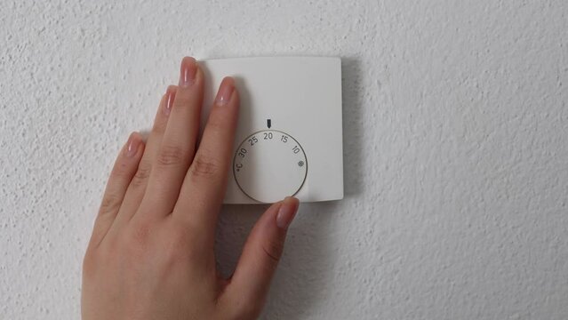 Female hand turns on central Heating thermostat, control dial adjustment. Stops at 20 degree Celsius. Saving money and electricity