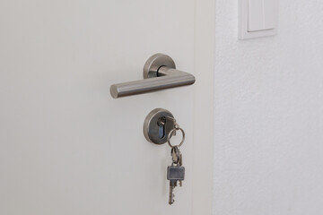 Closed door with keys in the lock. White door and metal handle