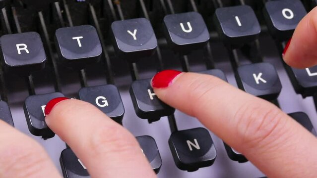 fingers with red nail polish of the young woman typing the keys on the keyboard of the vintage typewriter in the office