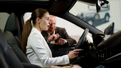 Satisfied happy caucasian female client customer woman sitting at the wheel of new car doing...