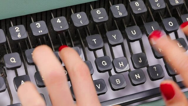 fingers with red nail polish of the young secretary typing the keys on the keyboard of the vintage typewriter in the office