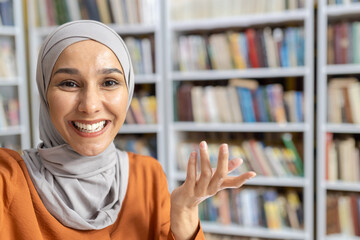 A cheerful woman in a hijab engages in a lively conversation on her phone, gesturing with her hand,...