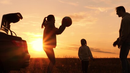 Family playing with ball near car at sunset, silhouettes. Father, mother, daughter throwing ball in circle, laughing, having fun joyful good time in field, creating pleasant unforgettable memories. - obrazy, fototapety, plakaty