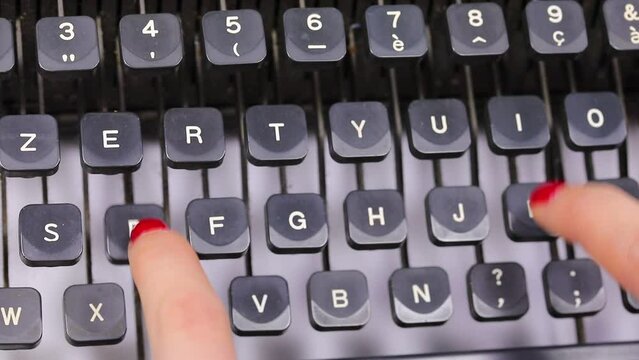 long fingers with red nail polish of the secretary typing the keys of the vintage typewriter in the office