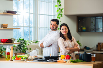 Indian asian young couple posing for photo in kitchen with hands folded.
