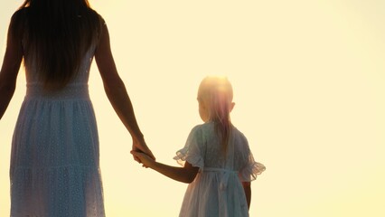 Family mother and daughter walking outdoor bright sun sky nature landscape enjoy freedom closeup back view. Elegant woman and girl kid in white dress going holding hands at sunlight sunset sunrise - obrazy, fototapety, plakaty