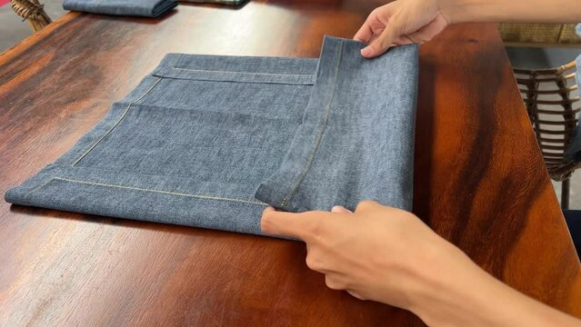 Folding new linen dinner napkin on a white wooden table. Fold gray cloth napkins