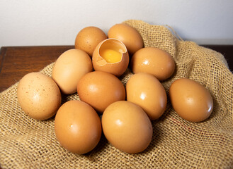 brown eggs on burlap, one egg is broken and the yolk is visible. Kitchen background