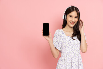 Young smiling Asian woman holding and showing blank screen mobile phone application isolated on pink background, Asian Thai model