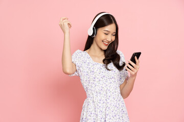 Happy Asian woman using mobile phone and wireless headphone isolated on pink background - 787348327