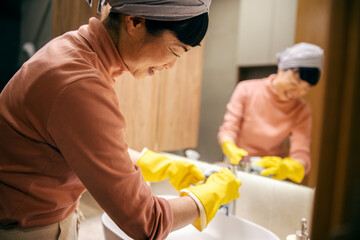 A middle aged japanese housewife is cleaning bathroom sink at home.
