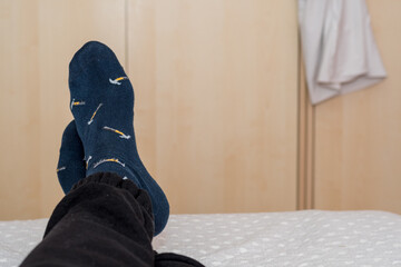 Man's feet crossed at the edge of the bed, relaxing in the room, nice blue socks.