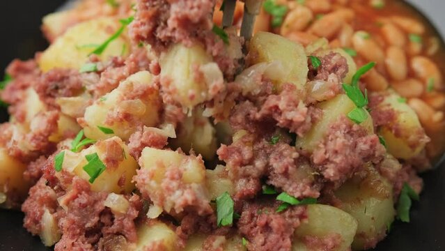 Eating Corned beef hash with potatoes and beans in tomato sauce