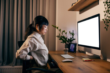 Side view of a japanese businesswoman working late at home office and having back ache. - obrazy, fototapety, plakaty
