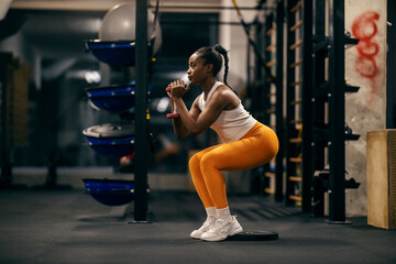 Side view of a black strong sportswoman exercising with weights in a squat position.