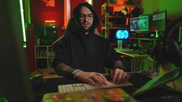 Hacker writing code cracking computer. Man programmer in hoodie cracks system, using computer in dark room. Hacker attack, internet, virus infected software, dark web, cyber security concept.