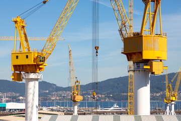This image showcases several large yellow industrial cranes towering over a construction site with a clear blue sky