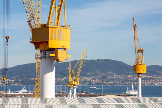 This image showcases several large yellow industrial cranes towering over a construction site with a clear blue sky