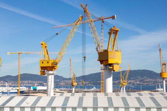 This image showcases several large yellow industrial cranes towering over a construction site with a clear blue sky