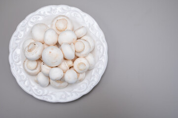 White champignon mushrooms fresh uncooked on white ceramic plate copy space