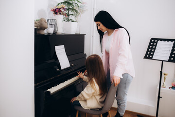 Young student learning to play piano together with teacher teaching her in music class