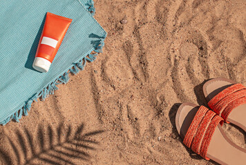 Bright summer beach vacation or travel lifestyle concept flat lay with suncream and a flip flops on the sand. Top view. Copy space