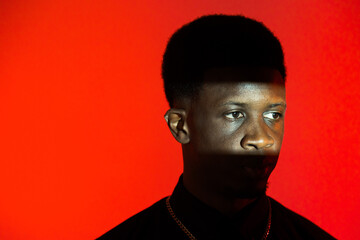 A black man is standing against a vibrant red background while wearing a necklace.