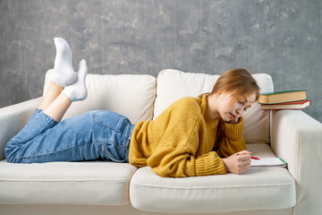 a dreamy young woman is lying on the sofa and drawing in a notebook. drawing in a comfortable...