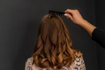 A woman with long brown hair is getting her hair brushed by another person. The brush is black and...