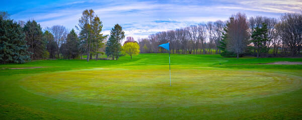 Panoramic landscape over the lush green fairway with flag in springtime