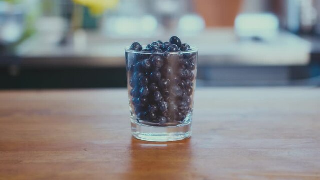 Close up of freshly washed blueberries in a glass on a wooden table in the kitchen. Defocused bright background. Vegan meal. High quality 4k footage