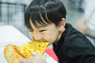 Asian boy eating pizza deliciously by pulling out the pizza by mouth.