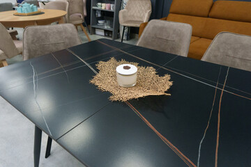 Black wooden table complete with beige wooden chairs with soft fabric upholstery. White candle on the table