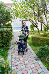 Smiling mother pushing little girl in stroller along path in garden