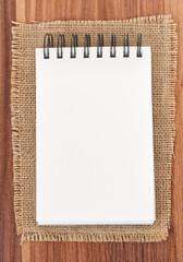 Notepad on jute burlap - wooden background. Notepad on white background - top view.