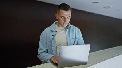 A focused young man studying on his laptop in a modern university library interior.