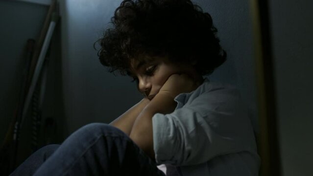 Emotionally abused young boy sits in a dark room