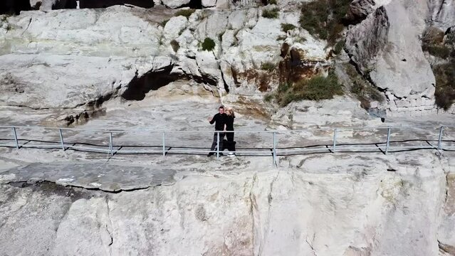A couple waves from the ancient rock-hewn town of Vardzia, a famous touristic landmark in Georgia, captured by a drone.