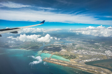 "Above the Horizons: An aerial vista captures Oahu, Hawaii, with the airport below, framed by billowing clouds, a vast expanse of blue sky, and the distant shimmer of ocean waters"