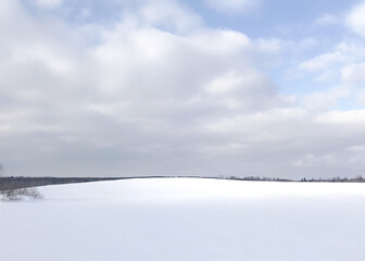 A small rise in a snow covered pasture topped by a sky of fluffy, white clouds creating a white on white landscape