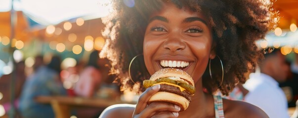 Happy young woman with curly hair holding a burger at an outdoor festival.