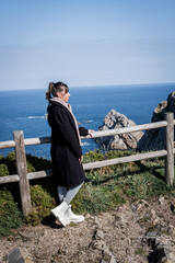 Brown-haired woman with braided hair gazes at stunning Cabo de Peñas cliffs in Asturias.
