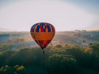 Colorful hot air balloon takes off from green park in small european city at summer sunrise