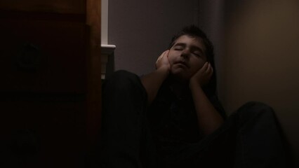 Young sad boy covers his ears as he listens to parents fighting in another room