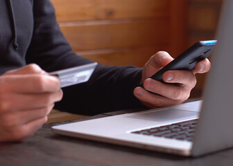Businessman in a black hoodie making online payment with credit card and smartphone, online shopping