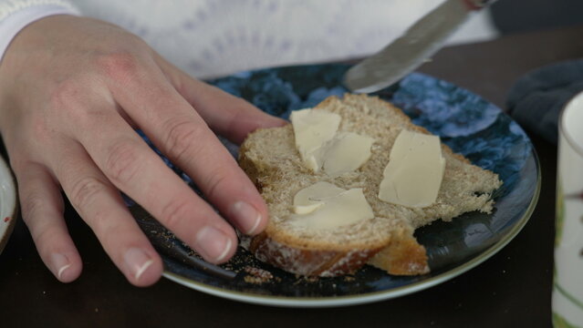 Close-up hand spreading butter on slide of bread for breakfast nutrition. Knife spreads buter on carb food