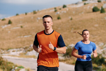 Fototapeta premium A couple dressed in sportswear runs along a scenic road during an early morning workout, enjoying the fresh air and maintaining a healthy lifestyle