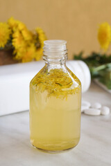  Bouquet of medicinal plant dandelion, essential oil in a small bottle on white marble table. Side view.       