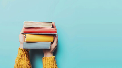 Female hands holding a stack of colorful books on a blue background. The concept of reading, education, and knowledge.