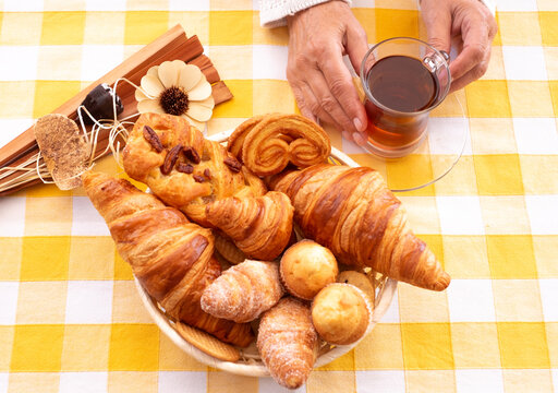 Sweet bakery products and croissant in the basket captured from above (top view, flat lay), woman hands holding a tea glass